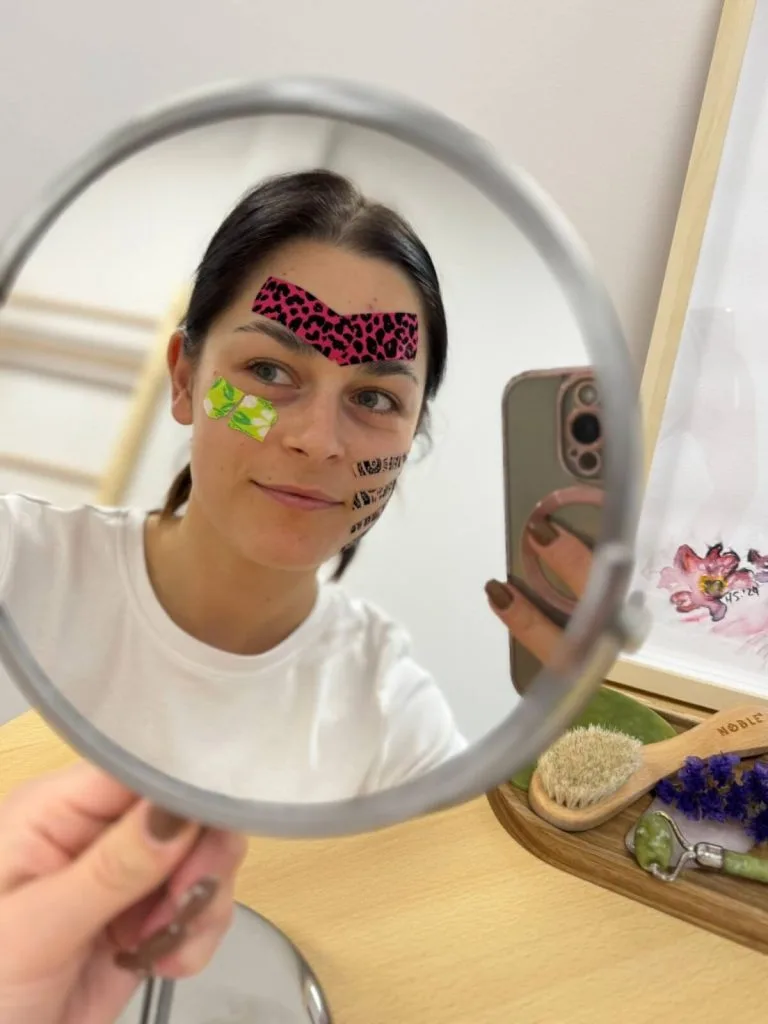 Pacjentka z taśmami do facetapingu na twarzy ogląda efekt w lusterku
